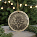 A round ceramic ornament with a detailed floral design is displayed against a blurred background of a Christmas tree with twinkling lights.