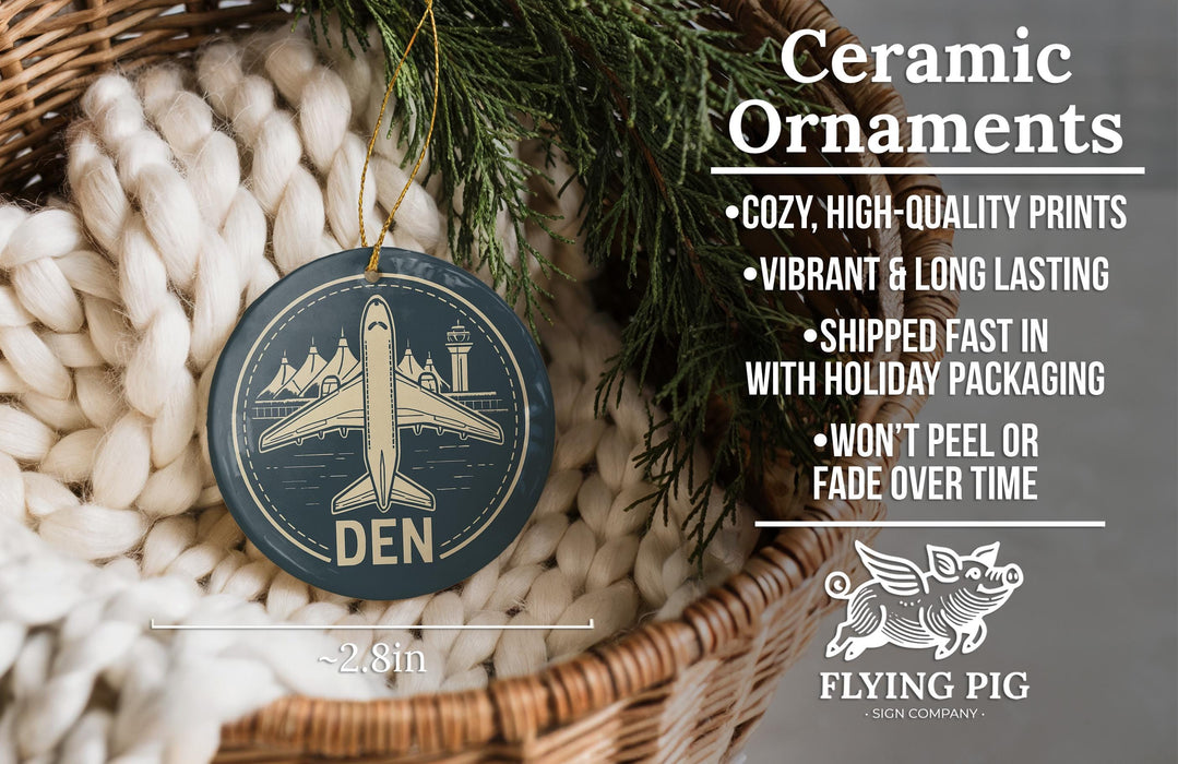 Ceramic ornaments, featuring a blue circular ornament with a white airplane and the word "DEN" printed on it, hanging from a wicker basket.