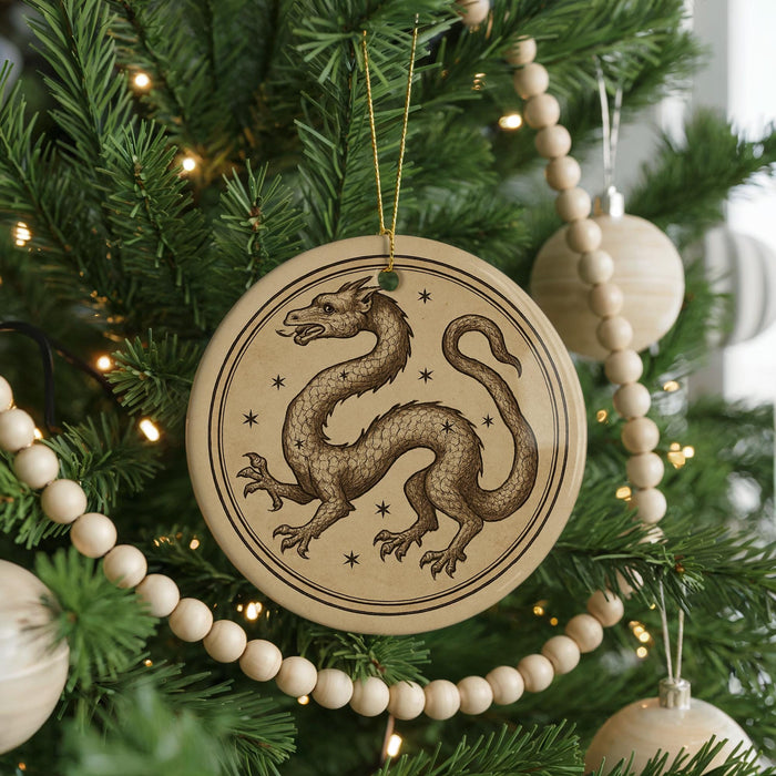 A round ornament featuring a dragon design is hanging on a Christmas tree, surrounded by other ornaments and lights.