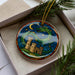 A decorative ornament in a box, featuring a castle and a dragon against a night sky background.