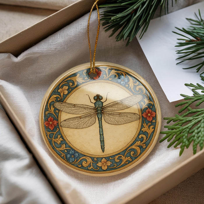 A decorative ornament featuring a dragonfly is displayed in a box, surrounded by pine branches and a white card.