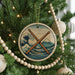 A Christmas tree decorated with ornaments, including a circular ornament with a wave and mountain design, and a wooden bead decoration.