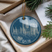 A blue ornament with a picture of a cathedral, featuring the word "DUR" on it, is placed in a box with pine branches.
