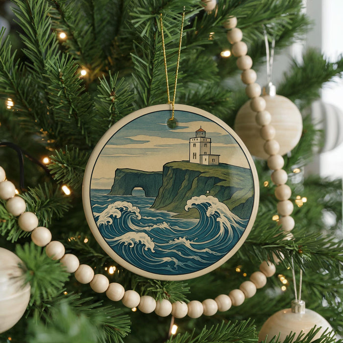 A Christmas tree decorated with a round ornament featuring a lighthouse on a cliff overlooking the ocean, surrounded by a string of beads.