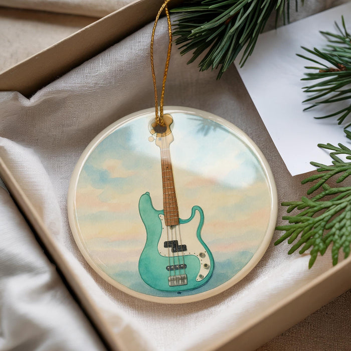 A round ornament featuring a blue bass guitar is displayed in a box, surrounded by pine branches.