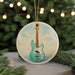 A round ornament featuring a blue bass guitar is displayed against a blurred background of a Christmas tree with twinkling lights.