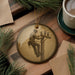 a round ornament with a black and white photograph of a man working on a telephone pole. The ornament is placed on a wooden surface, surrounded by pine branches and a cup of coffee.