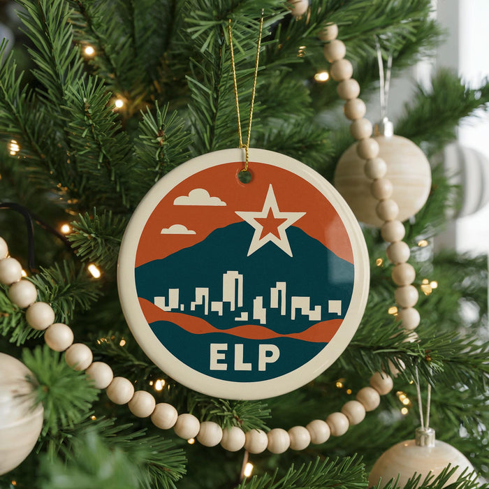 A Christmas tree decorated with ornaments, including a circular ornament with a cityscape and a star, as well as other ornaments and beads.