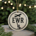 A white circular ornament with the letters "EWR" and a silhouette of the Statue of Liberty, hanging from a string.