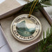 A circular ornament with the text "FIORDLAND NATIONAL PARK NEW ZEALAND" printed on it, surrounded by pine branches.