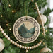 A Christmas tree decorated with ornaments, including a circular ornament with a mountain landscape and the text "Fordland National Park New Zealand".
