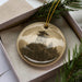 A decorative ornament featuring a lighthouse on a mountain, surrounded by pine branches and pine needles.