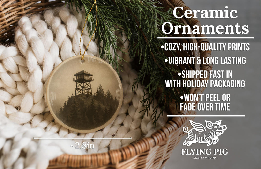 Ceramic ornaments, featuring a black and white image of a tower surrounded by pine trees, are displayed in a wicker basket.