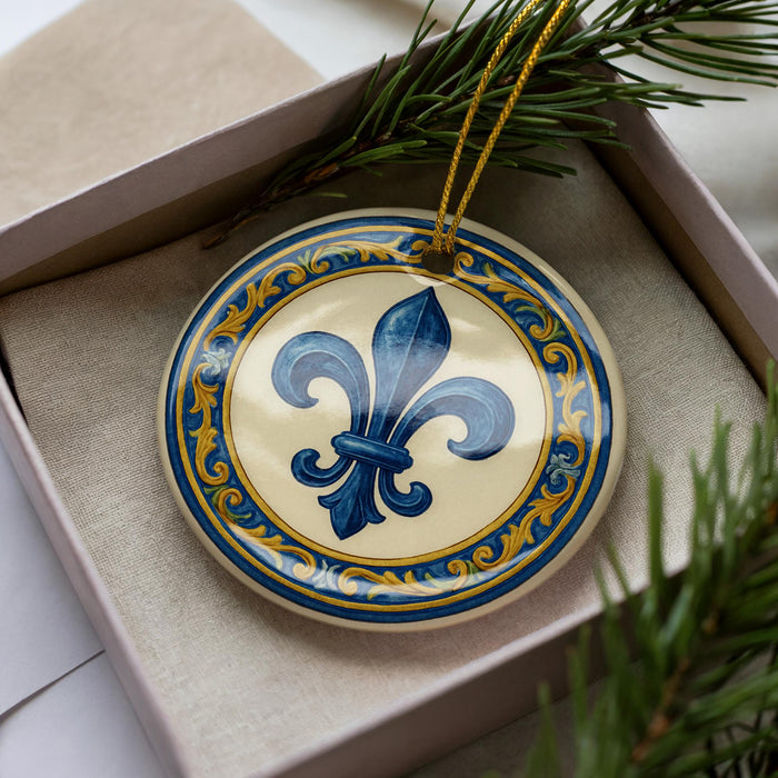 A decorative ornament in a box, featuring a blue fleur-de-lis design with gold and blue accents.