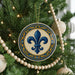 A Christmas tree decorated with ornaments, including a large circular ornament with a blue fleur-de-lis design and wooden beads.