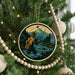A Christmas tree decorated with ornaments, including a circular ornament depicting a person fishing in a river with mountains in the background.