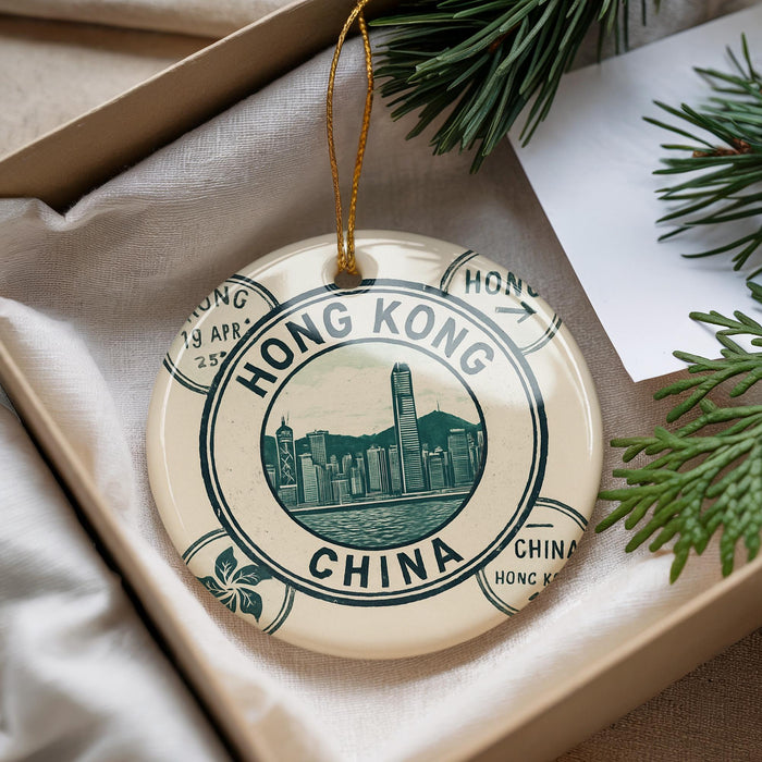 A decorative ornament featuring the text "HONG KONG CHINA" and a cityscape illustration, placed in a box with pine branches.
