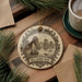 a decorative ornament with a sailing boat and mountains in the background, placed on a wooden surface.
