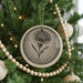 A Christmas tree decorated with a circular ornament featuring a large flower, surrounded by beaded ornaments and twinkling lights.