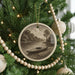 A Christmas tree decorated with ornaments, including a circular ornament featuring a kayak scene, surrounded by lights and greenery.