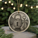 A round ceramic ornament with a lock and key design, featuring a keyhole and a padlock, is displayed against a blurred background of Christmas lights.
