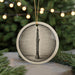 A circular ornament featuring a black and white illustration of a clarinet is displayed in front of a blurred background of Christmas lights.