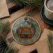 A decorative ornament featuring an organ, surrounded by pine branches and a cup of coffee on a wooden surface.