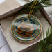 A decorative ornament featuring an organ, displayed in a box with pine branches.