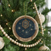 A Christmas tree decorated with ornaments, including a circular ornament with a starry night sky design and the word "Pleiades" written on it.