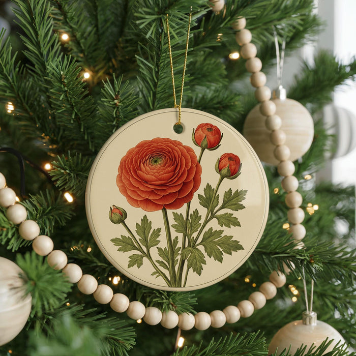 A round ornament with a red rose and green leaves is hanging on a Christmas tree, surrounded by white beads and greenery.