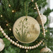 A Christmas tree decorated with ornaments, including a circular ornament featuring a snowflake design and a church in the background.