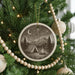 A Christmas tree decorated with ornaments, including a circular ornament with a camping scene and a string of wooden beads.