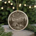 A round ceramic ornament depicting a camping scene with a tent, campfire, and mountains in the background, surrounded by pine trees and a starry night sky.