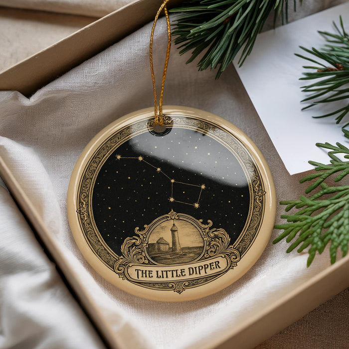 A decorative ornament with a starry night sky design and a lighthouse in the center, placed in a box with pine branches.