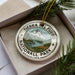 A circular ornament with the text "TIERRA DEL FUEGO NATIONALL PARK ARGENTINA" printed on it, surrounded by a border and a mountain landscape.