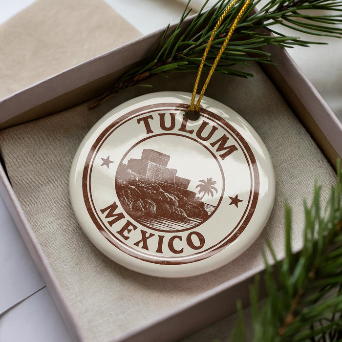 A circular ornament with the text "TULUM MEXICO" printed on it, surrounded by a border and a small illustration of a building and palm trees.