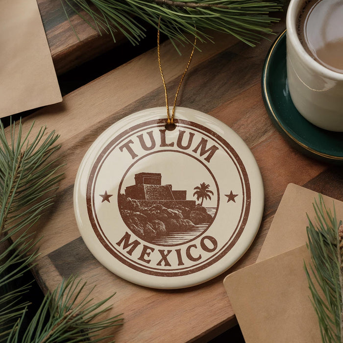 A circular ornament with the text "TULUM MEXICO" printed on it, surrounded by pine branches and a cup of coffee on a wooden surface.
