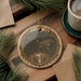 A decorative ornament featuring a bear constellation on a wooden surface, surrounded by pine branches and a cup of coffee.