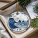 A decorative ornament in the shape of a plate with a blue and white design depicting a coastal scene, featuring islands and waves.