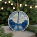 A decorative ornament featuring a blue and white design of the Washington Monument, with a string of lights in the background.