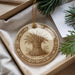 A decorative ornament with a wheat stalk design is displayed in a box, surrounded by pine branches and a white card.