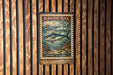 A metal stamp with a picture of a fish and text, hanging on a wooden wall.