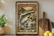 A vintage-style metal sign depicting a salmon leaping out of a river, with the text "ATLANTIC SALMON" and "SALMO SALAR" printed on it. The sign is mounted on a wall, and there are some kitchen utensils and a potted plant visible in the background.