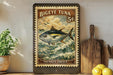 A vintage-style stamp depicting a large tuna fish, with the text "BIEYE TUNA 5¢ THUNNUS OBSUS" printed on it. The stamp is displayed on a shelf next to a wooden cutting board and some kitchen utensils.