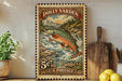 A vintage postage stamp featuring a fish, likely a trout, in a river setting, with mountains in the background. The stamp is displayed on a shelf next to a wooden cutting board and some lemons.