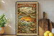 A framed vintage-style stamp depicting a golden trout, with a mountain landscape in the background.