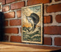 a framed painting of a sailfish leaping out of the water, set against a brick wall.