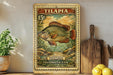 A vintage postage stamp featuring a colorful illustration of a fish, with the text "Tilapia" and "Postage Freshwater Fish" printed on it. The stamp is displayed on a shelf next to a wooden cutting board and some kitchen utensils.