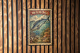 A metal stamp featuring a fish, likely a Wahoo, against a wooden background.