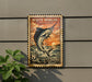 A vintage White Marlin postage stamp is displayed on a wall, featuring a large illustration of a white marlin fish leaping out of the water.